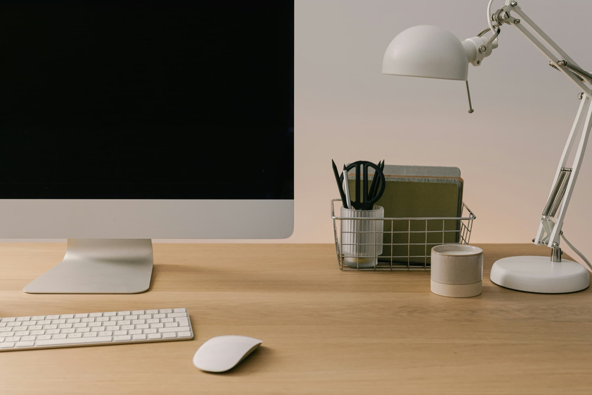 Bureau de télétravail en bois avec écran, clavier, souris, lampe articulée blanche et fournitures rangées